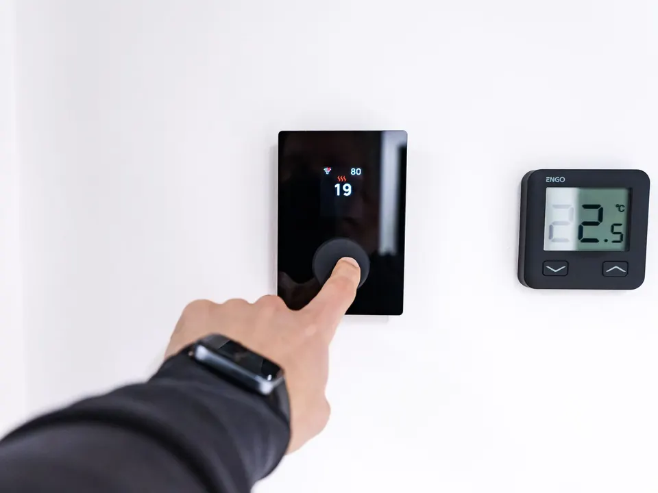 Hand adjusting a digital wall thermostat